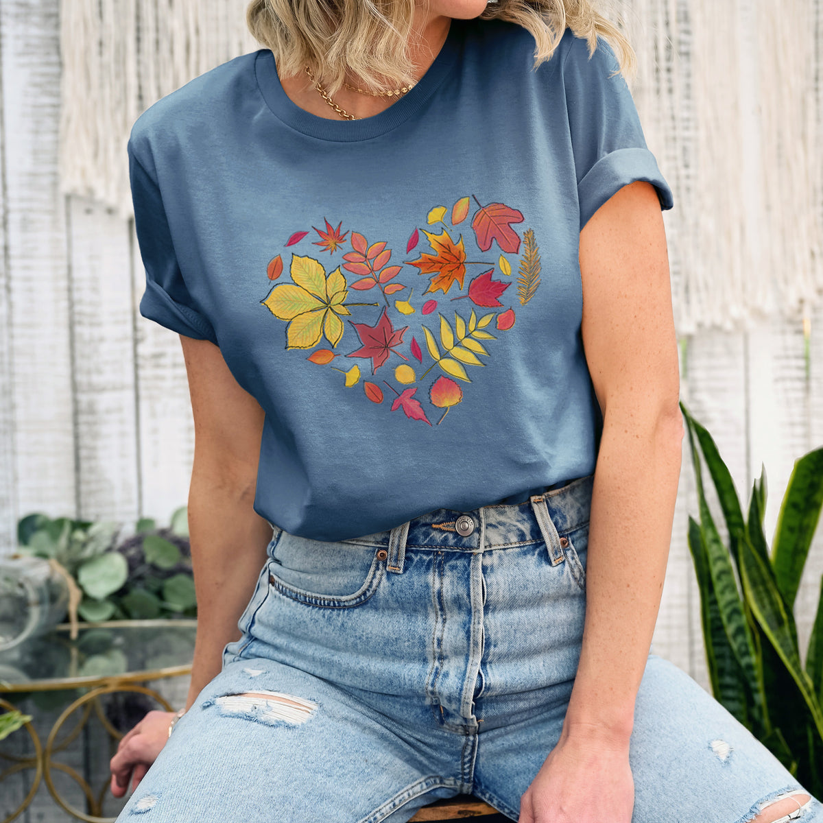 Woman wearing a steel blue lightweight cotton t-shirt printed with a full-color heart shape made of autumn leaves in orange, red and yellow.