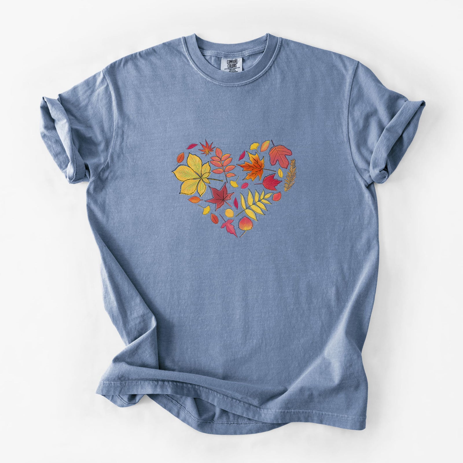 Blue jean Comfort Colors t-shirt laid flat, printed with a full-color heart shape made of autumn leaves in orange, red and yellow.