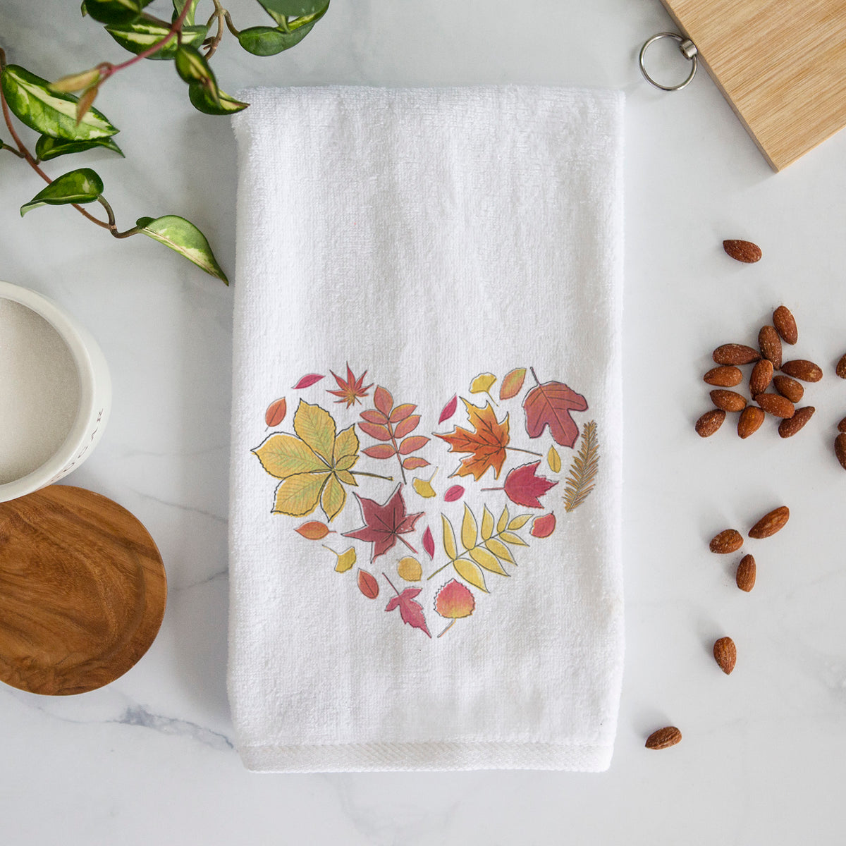 White hand towel printed with a full-color heart shape made of autumn leaves in orange, red and yellow.