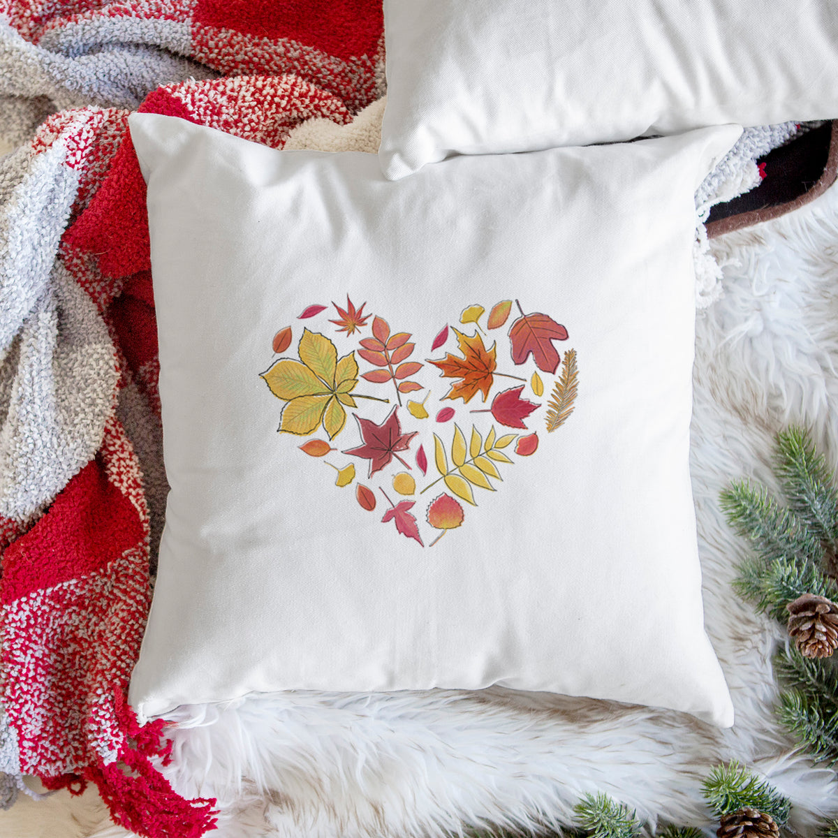 White pillow cover printed with a full-color heart shape made of autumn leaves in orange, red and yellow, on a woven chair.