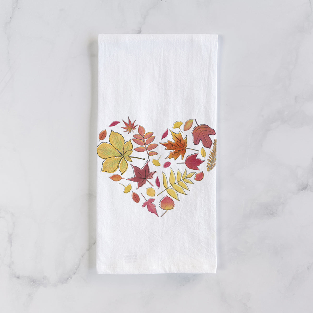 White cotton tea towel laid flat on marble, printed with a full-color heart shape made of autumn leaves in orange, red and yellow.