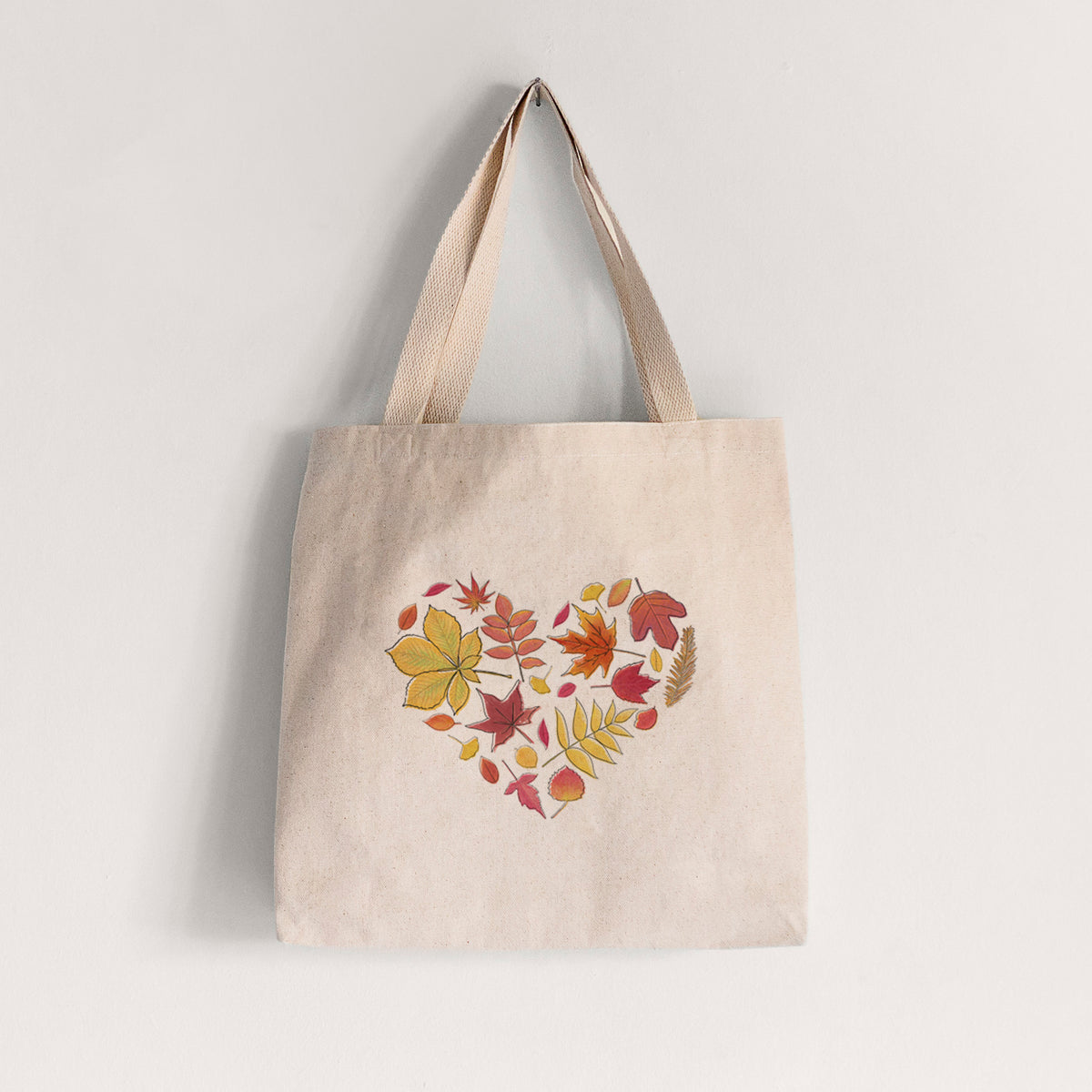 Natural canvas tote bag printed with a full-color heart shape made of autumn leaves in orange, red and yellow.