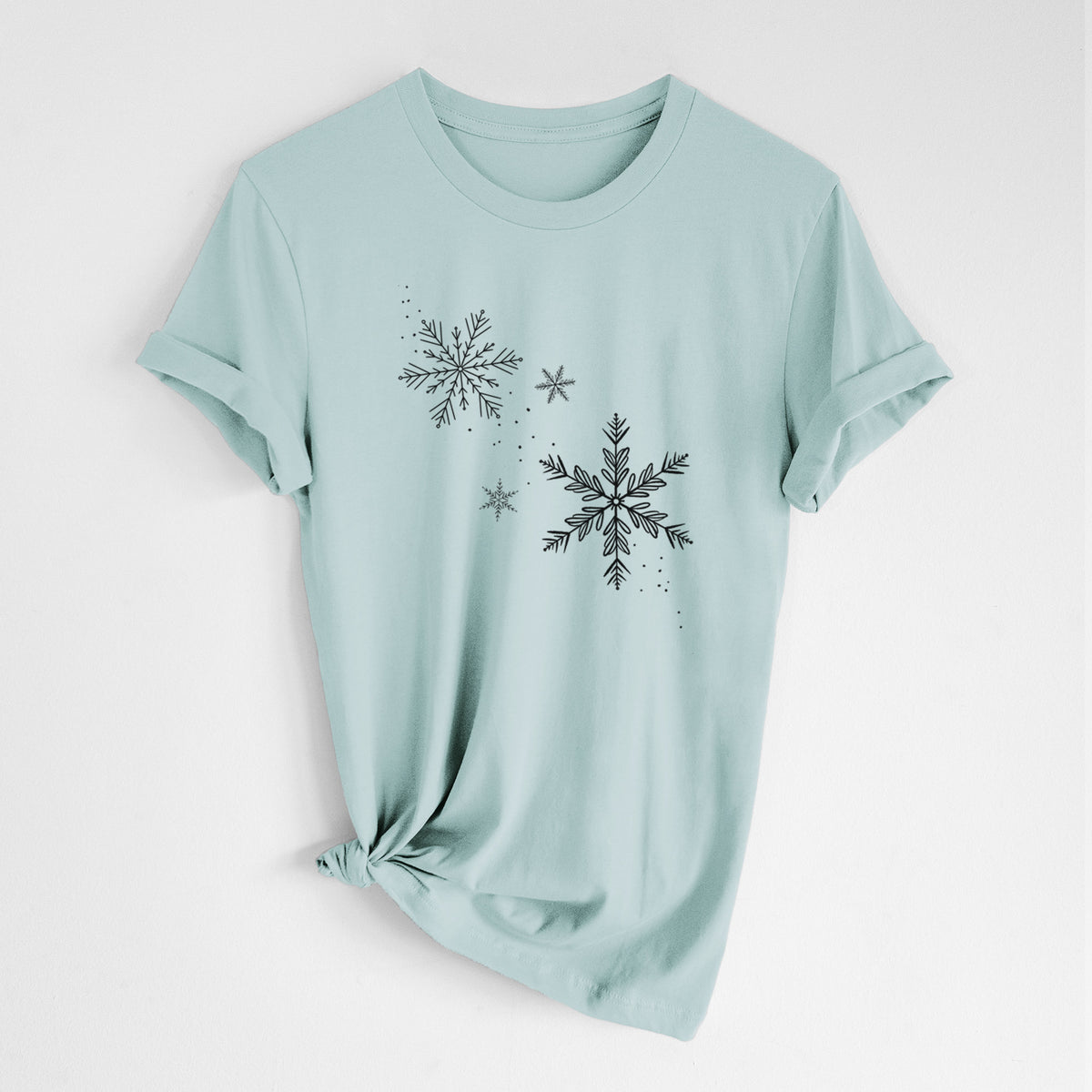 Dusty blue lightweight cotton t-shirt laid flat with the sleeves rolled, printed with delicate snowflakes of different sizes falling.