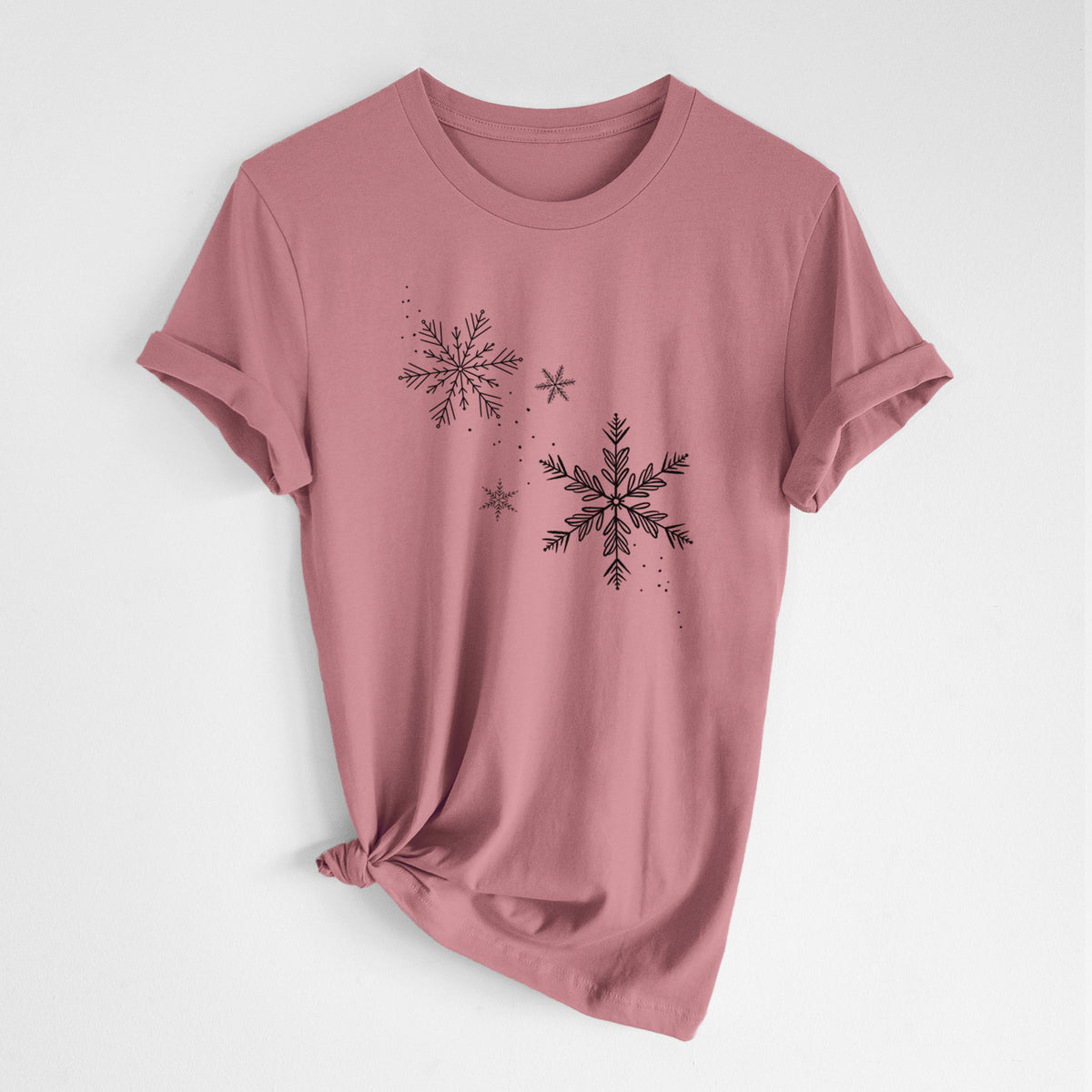 Mauve pink lightweight cotton t-shirt laid flat with the sleeves rolled, printed with delicate snowflakes of different sizes falling.