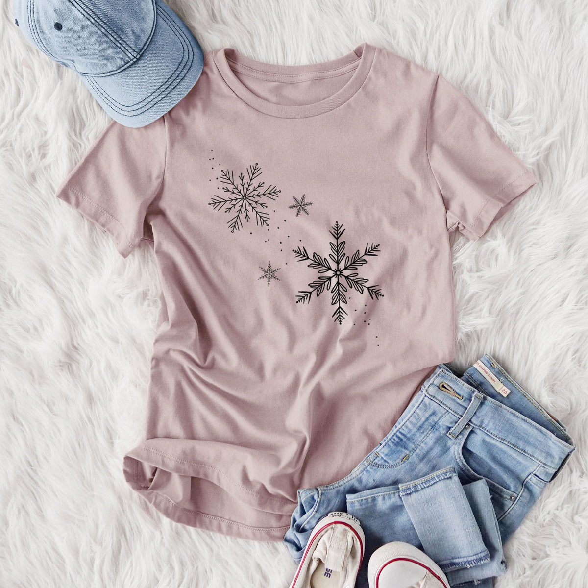 Women's relaxed fit cotton t-shirt printed with delicate snowflakes of different sizes falling, styled flat on a white faux fur rug with jeans.