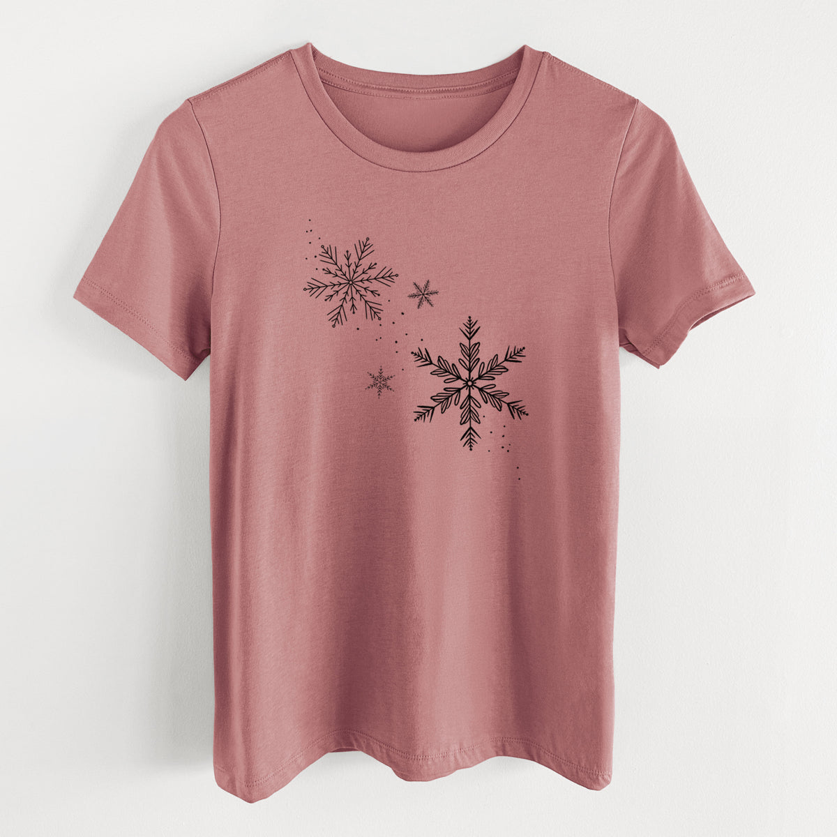 Mauve pink women's relaxed fit cotton t-shirt laid flat, printed with delicate snowflakes of different sizes falling.