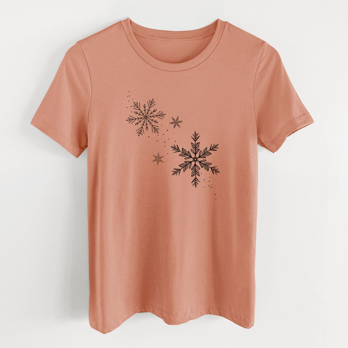 Terracotta orange women's relaxed fit cotton t-shirt laid flat, printed with delicate snowflakes of different sizes falling.