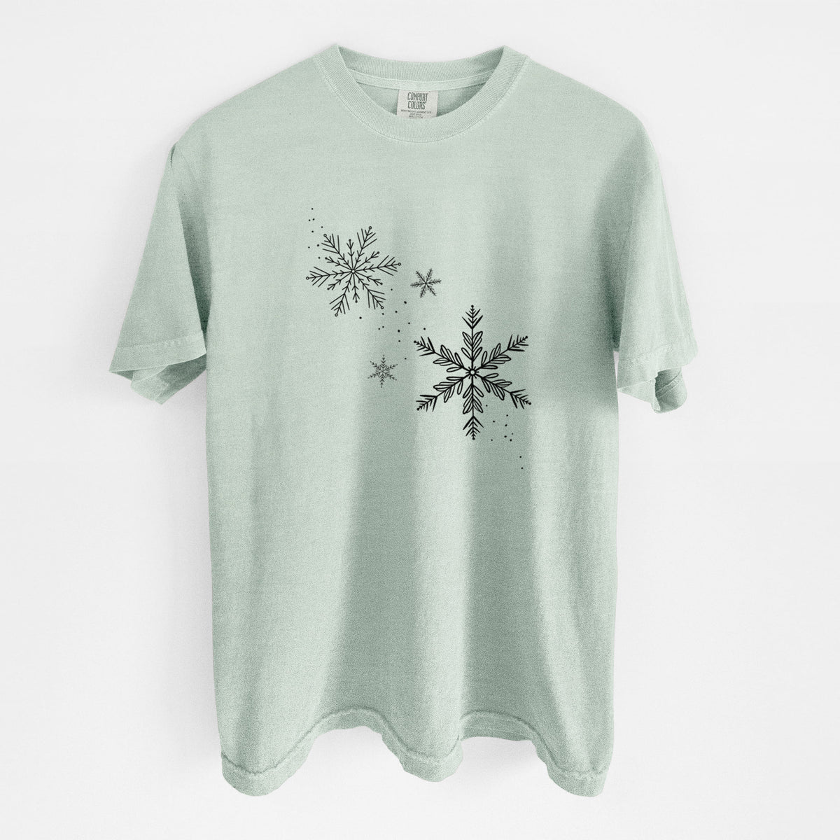 Bay green Comfort Colors t-shirt laid flat, printed with delicate snowflakes of different sizes falling.
