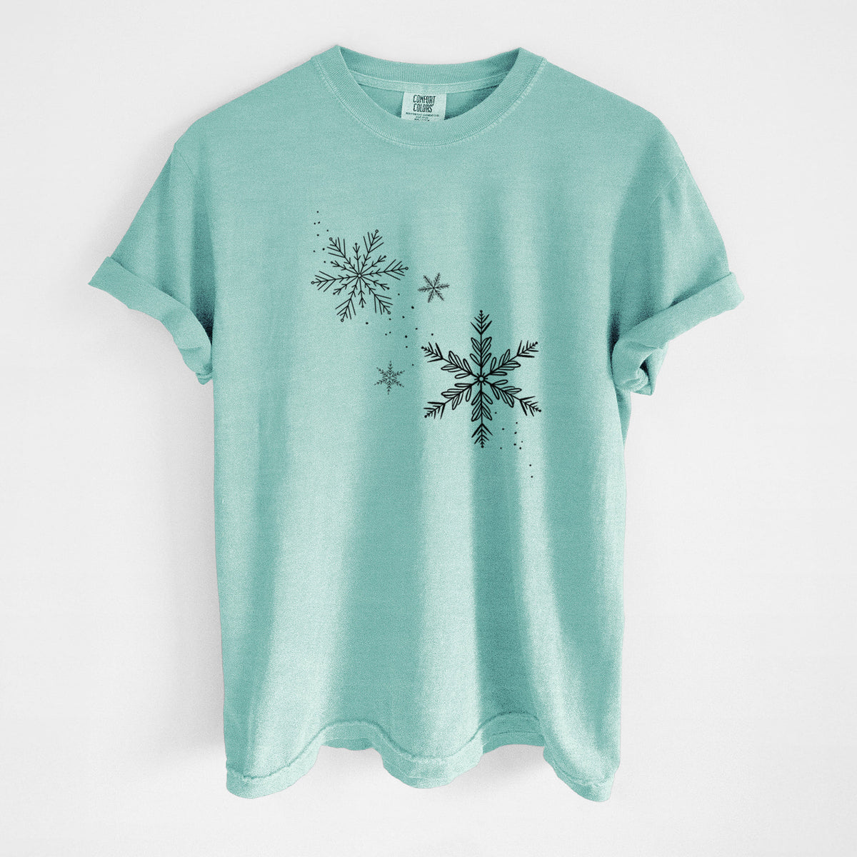 Chalky mint Comfort Colors t-shirt laid flat, printed with delicate snowflakes of different sizes falling.