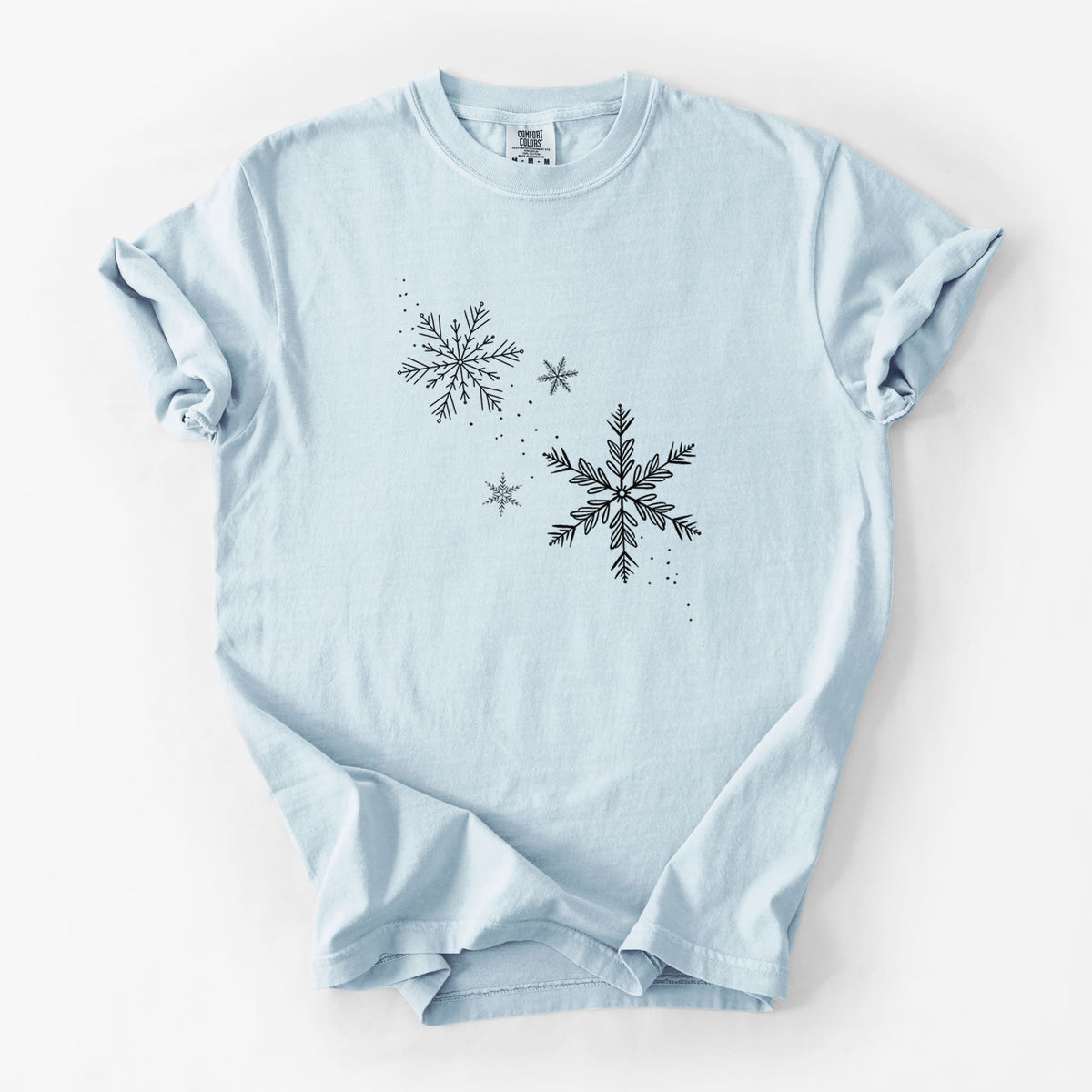 Chambray blue Comfort Colors t-shirt laid flat, printed with delicate snowflakes of different sizes falling.
