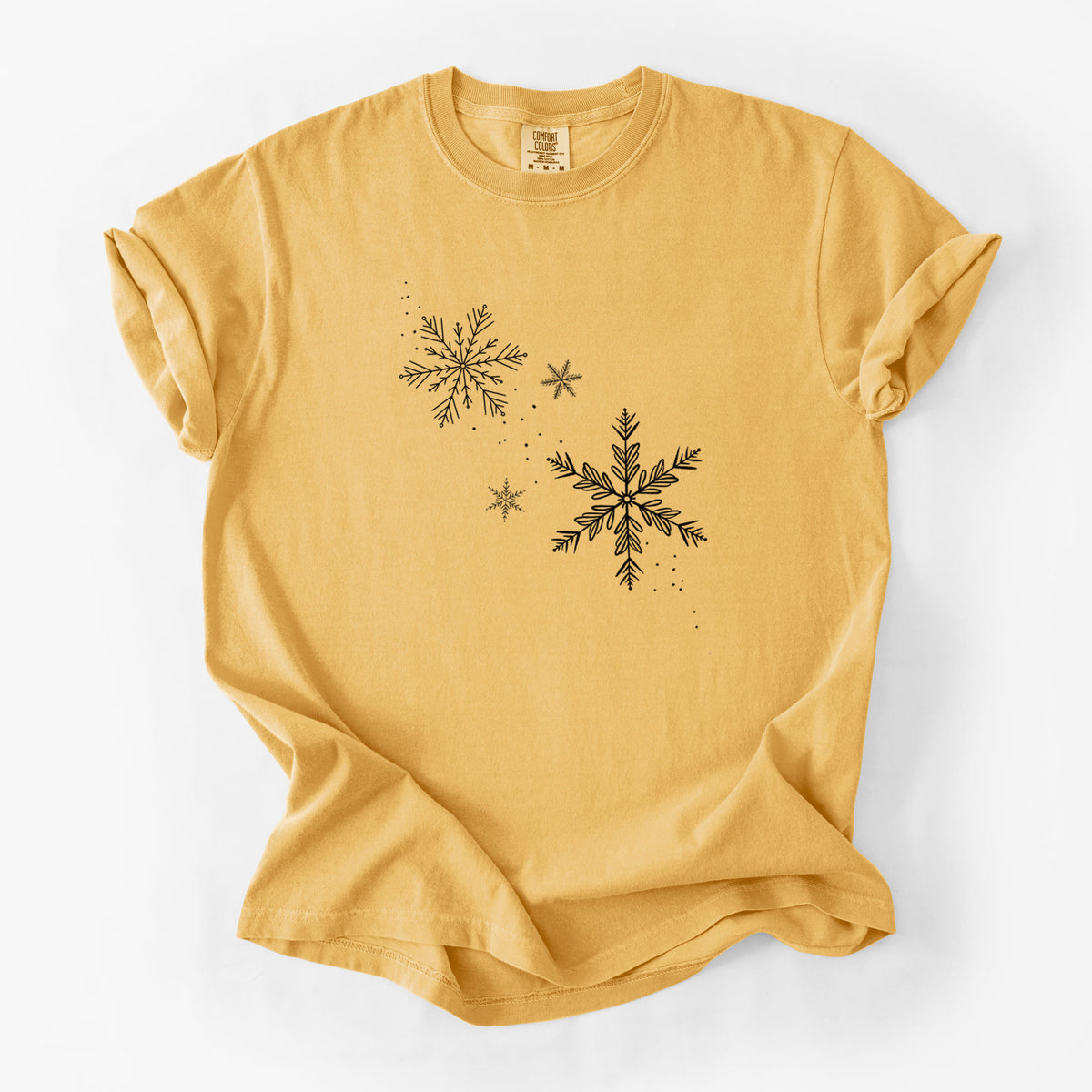 Golden wheat yellow Comfort Colors t-shirt laid flat, printed with delicate snowflakes of different sizes falling.