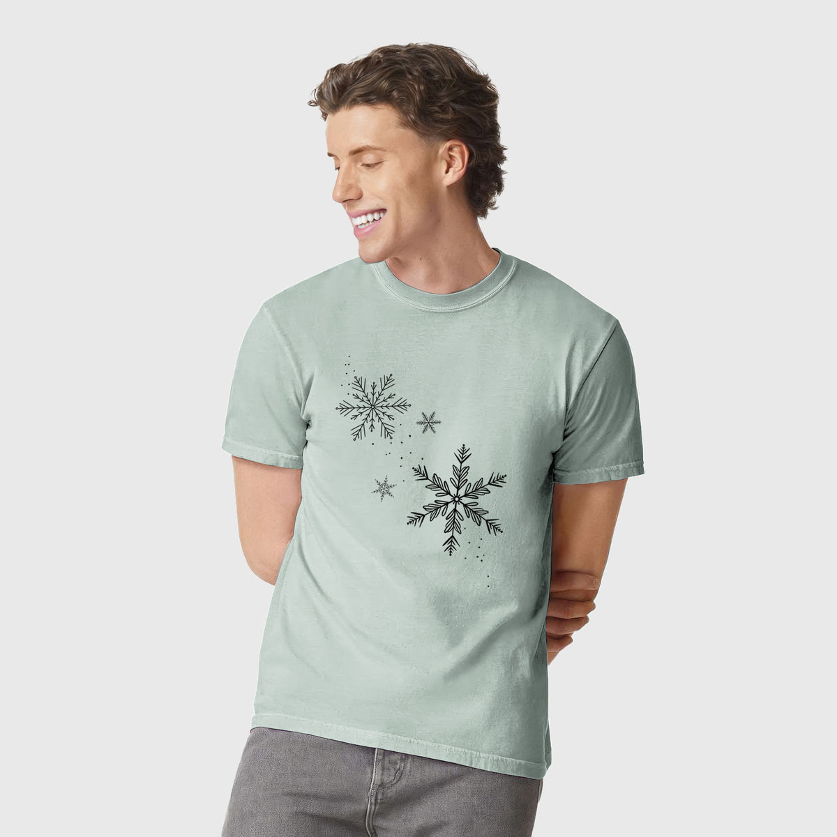 Man wearing a Comfort Colors t-shirt printed with delicate snowflakes of different sizes falling.