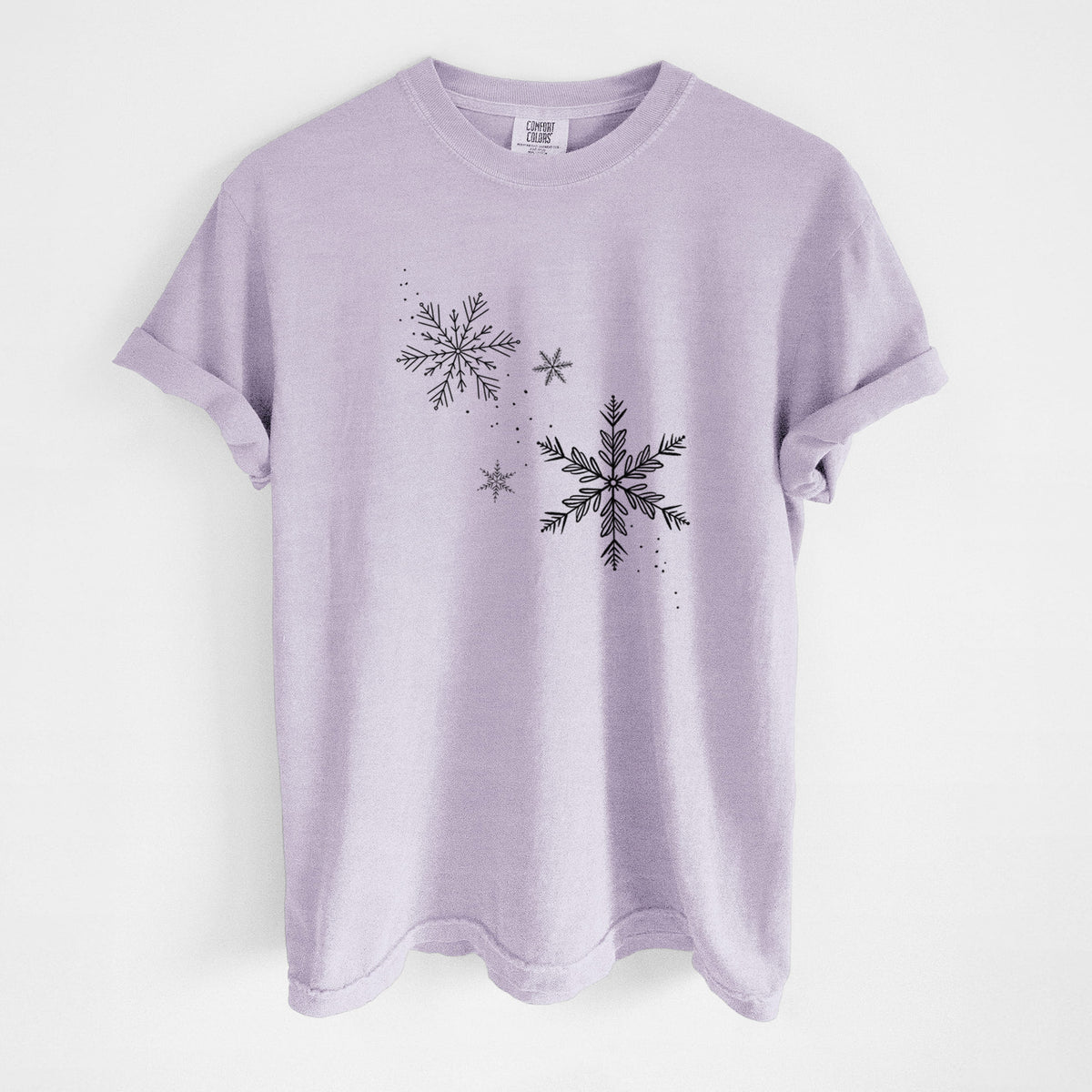 Orchid purple Comfort Colors t-shirt laid flat, printed with delicate snowflakes of different sizes falling.