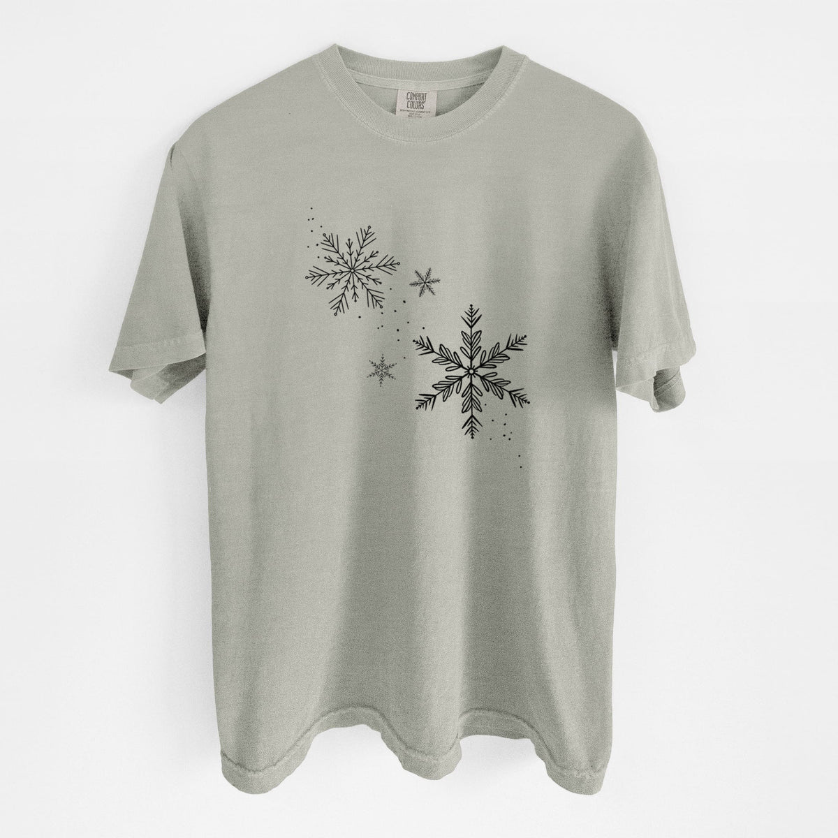 Sandstone beige Comfort Colors t-shirt laid flat, printed with delicate snowflakes of different sizes falling.