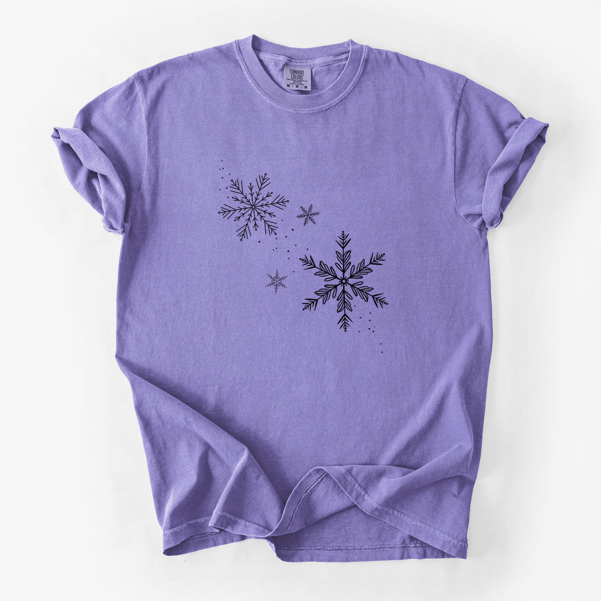 Violet purple Comfort Colors t-shirt laid flat, printed with delicate snowflakes of different sizes falling.
