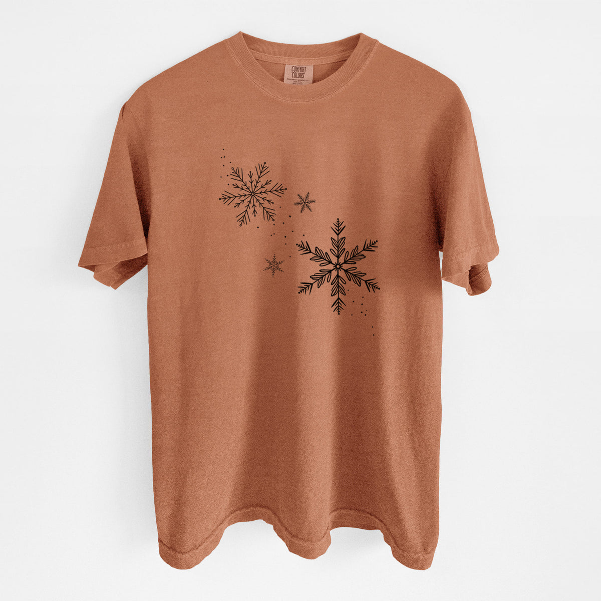 Yam burnt orange Comfort Colors t-shirt laid flat, printed with delicate snowflakes of different sizes falling.