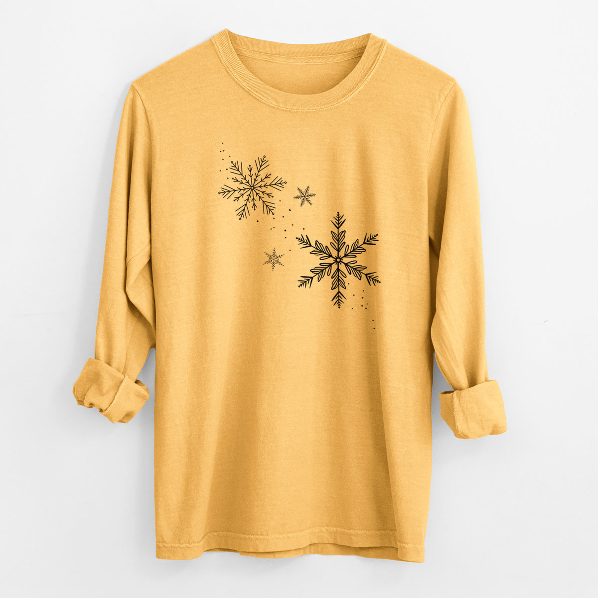 Golden wheat yellow Comfort Colors long sleeve shirt laid flat with the cuffs rolled, printed with delicate snowflakes of different sizes falling.