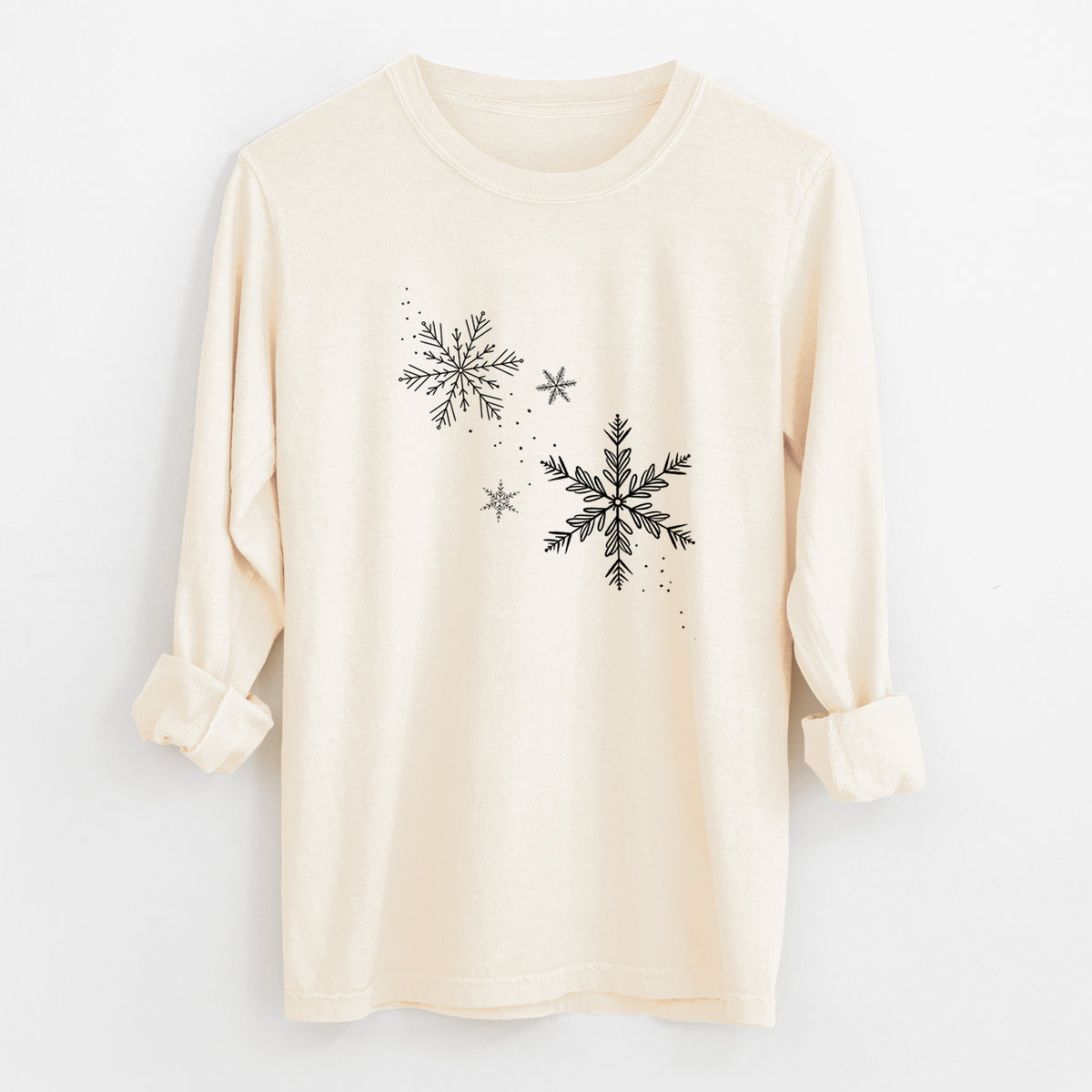 Ivory Comfort Colors long sleeve shirt laid flat with the cuffs rolled, printed with delicate snowflakes of different sizes falling.