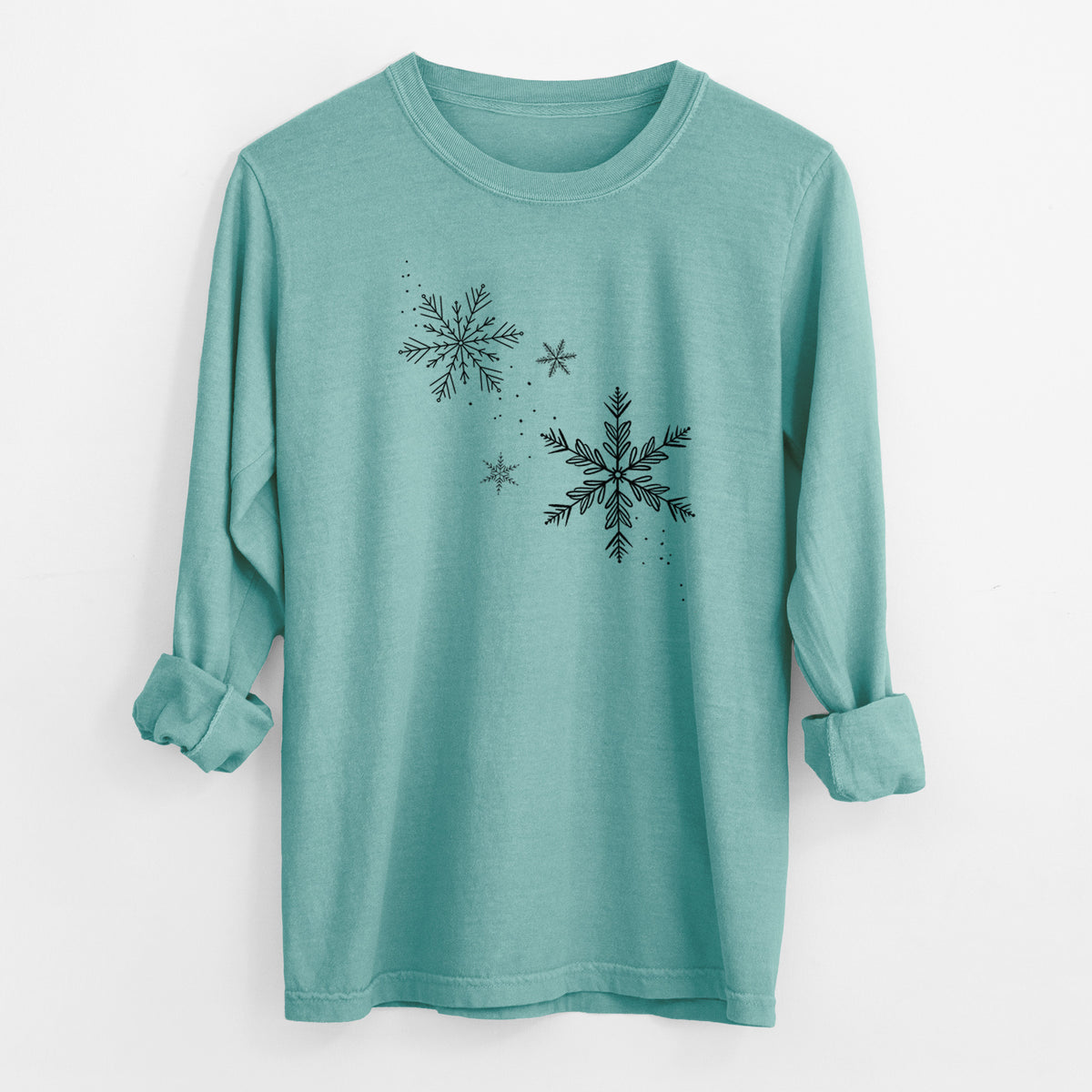 Reef green Comfort Colors long sleeve shirt laid flat with the cuffs rolled, printed with delicate snowflakes of different sizes falling.