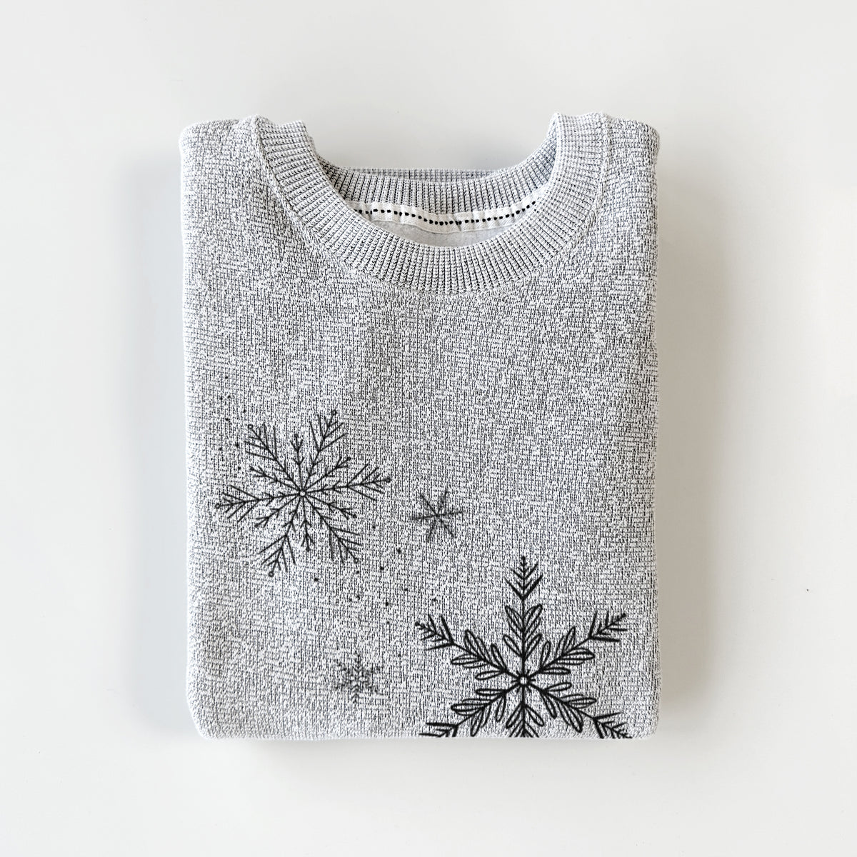 Salt and pepper knit sweatshirt printed with delicate snowflakes of different sizes falling, styled flat.