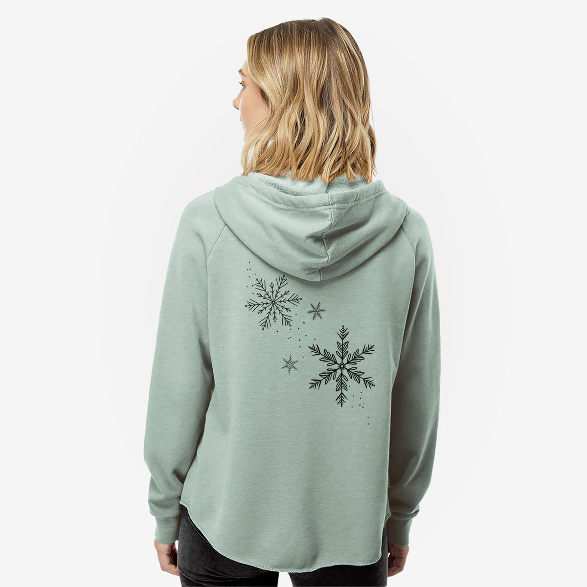 Woman wearing a sage green women's Cali Wave zip-up sweatshirt printed with delicate snowflakes of different sizes falling, seen from behind.