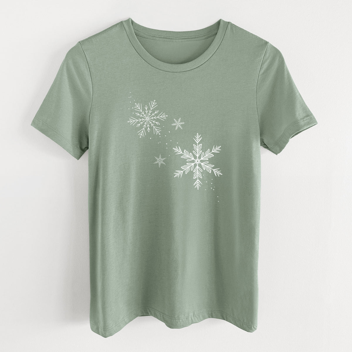 Sage green women's relaxed fit cotton t-shirt laid flat, printed with delicate white snowflakes of different sizes falling.
