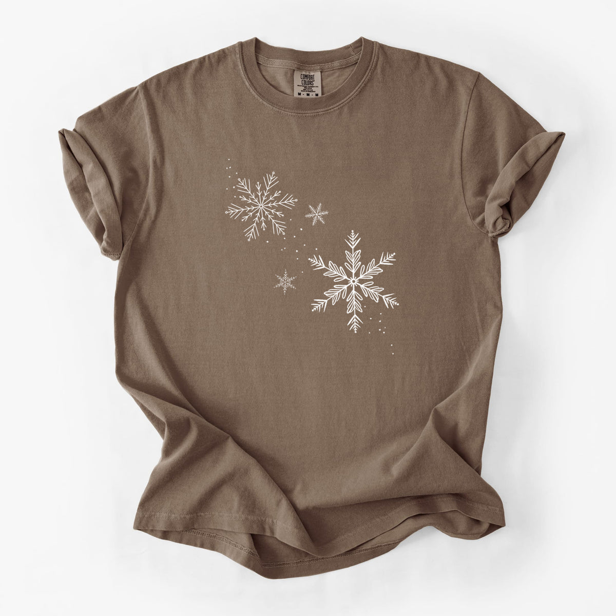 Espresso brown Comfort Colors t-shirt laid flat, printed with delicate white snowflakes of different sizes falling.