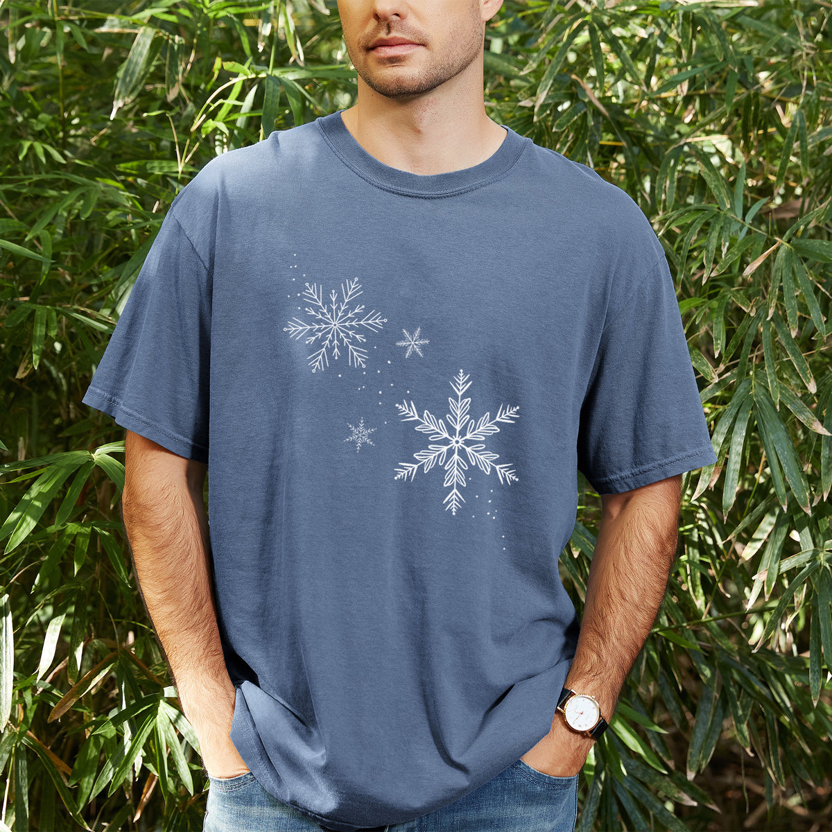 Man wearing a Comfort Colors t-shirt printed with delicate white snowflakes of different sizes falling, outdoors.
