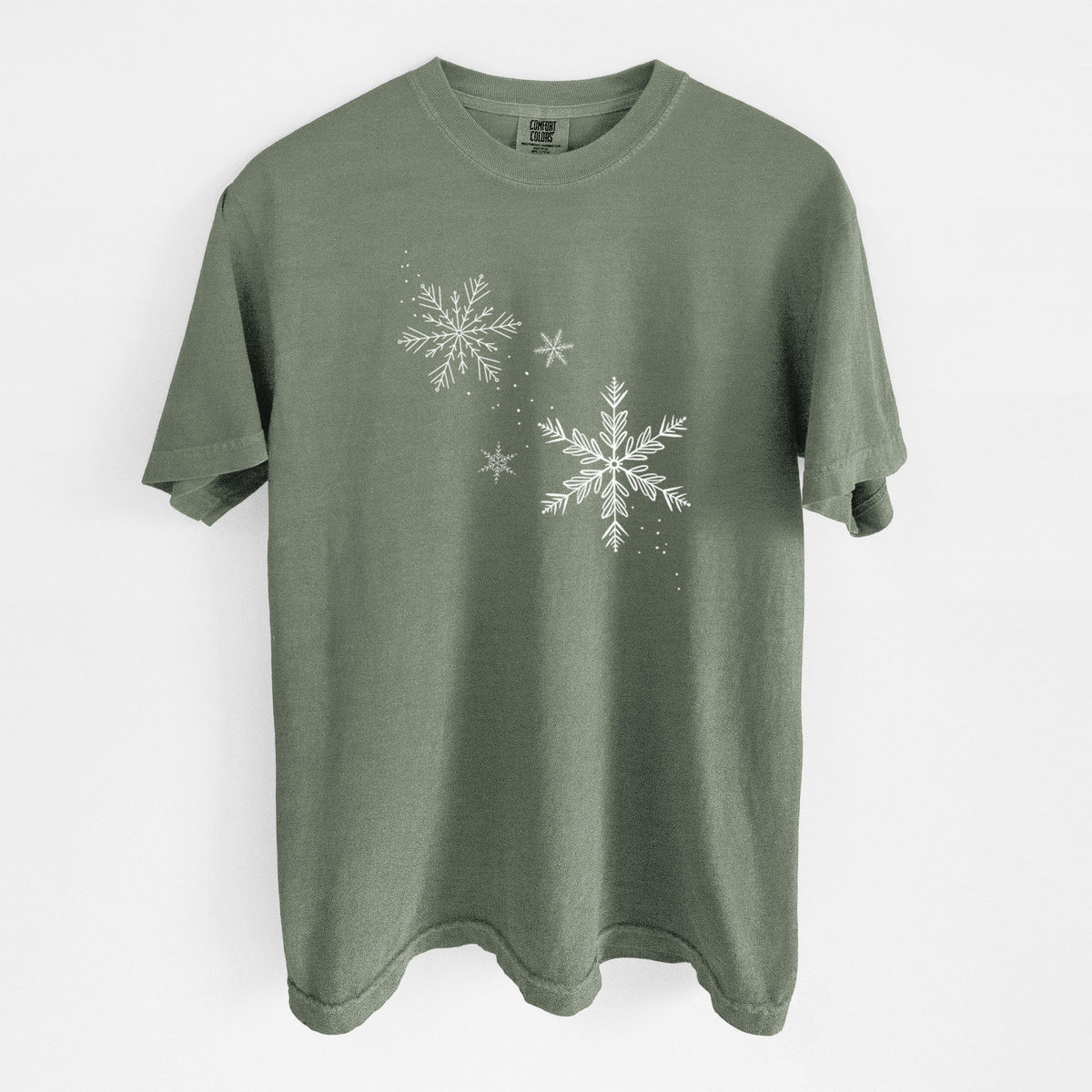 Moss green Comfort Colors t-shirt laid flat, printed with delicate white snowflakes of different sizes falling.