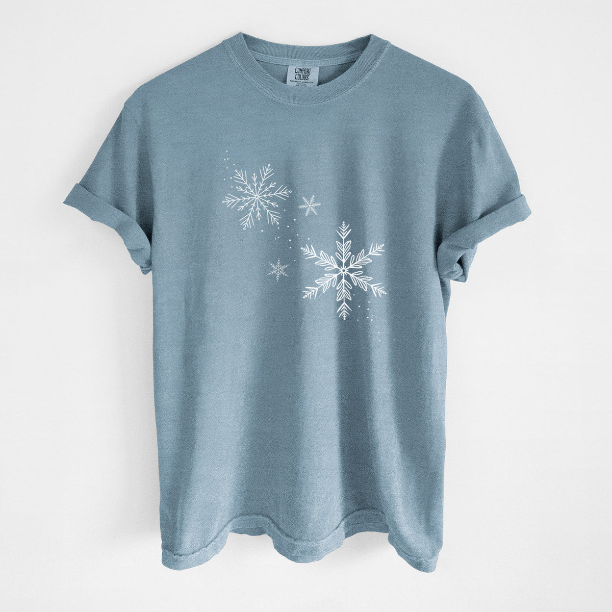 Steel blue Comfort Colors t-shirt laid flat, printed with delicate white snowflakes of different sizes falling.