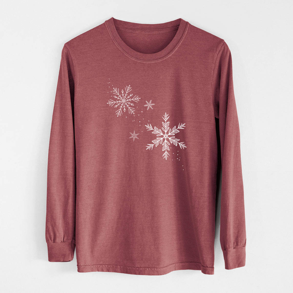 Brick red Comfort Colors long sleeve shirt laid flat, printed with delicate white snowflakes of different sizes falling.