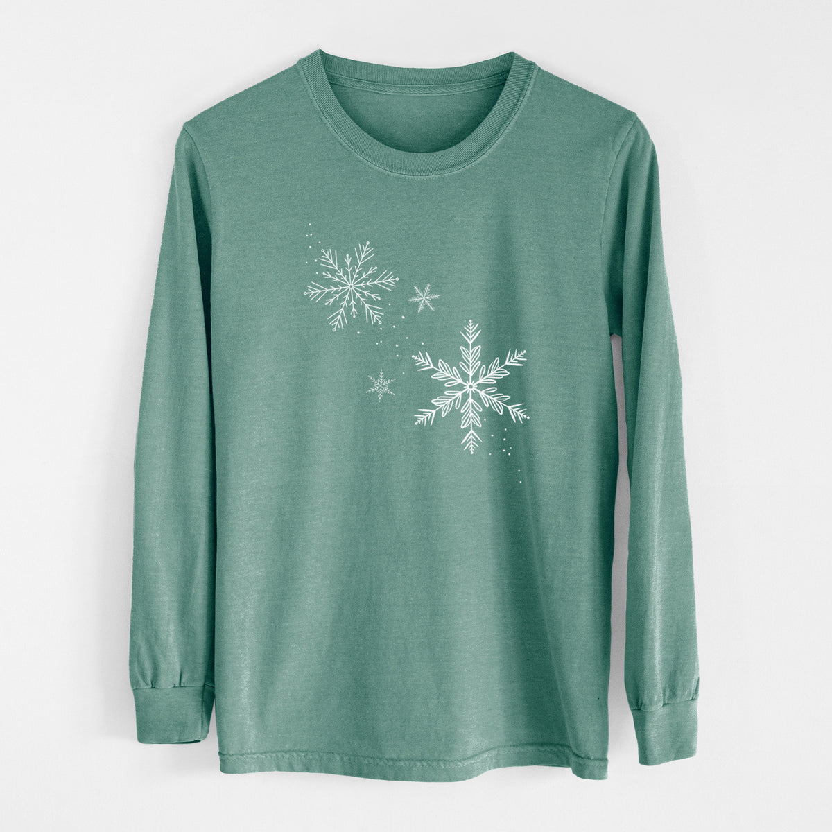 Pine green Comfort Colors long sleeve shirt laid flat, printed with delicate white snowflakes of different sizes falling.