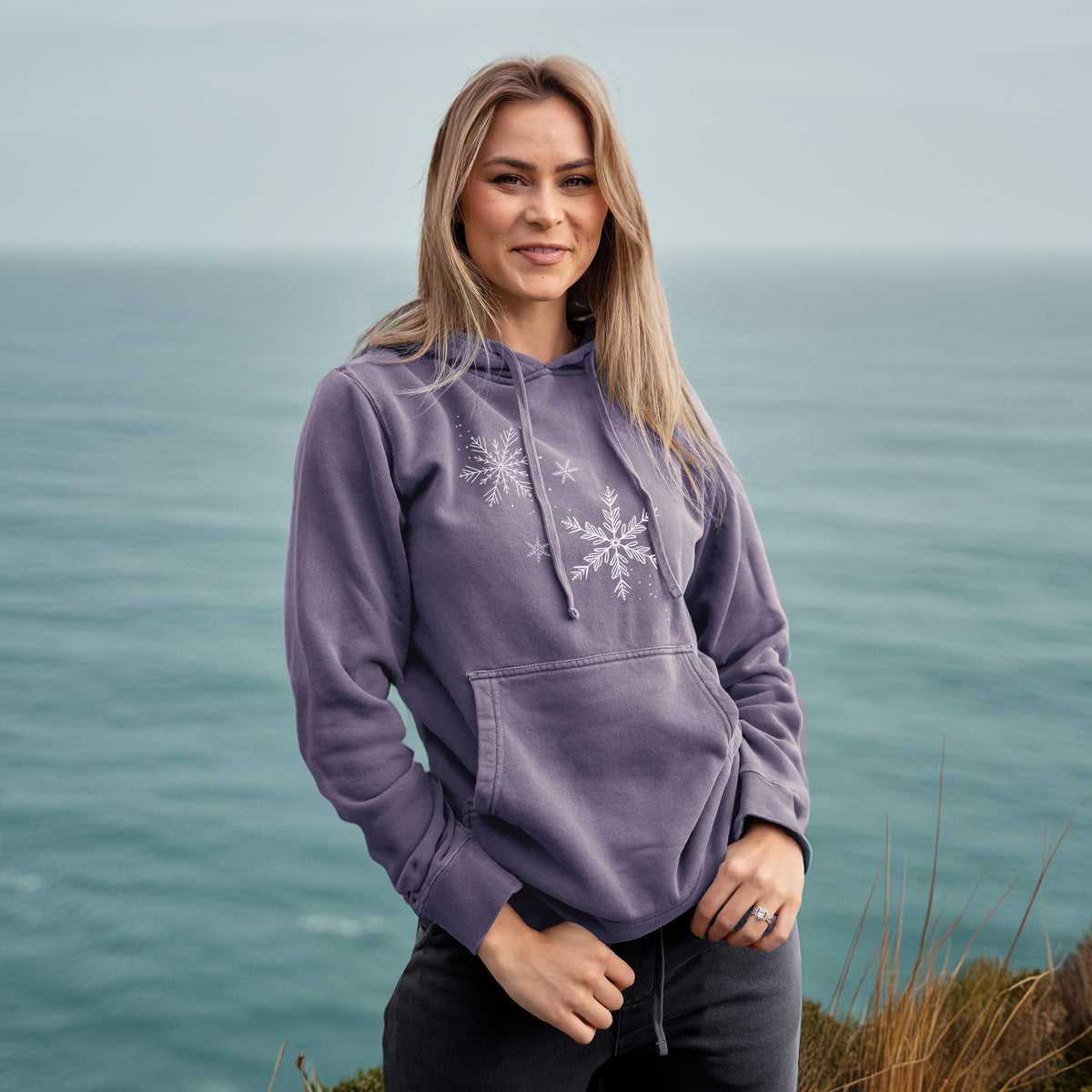 Woman wearing a plum purple pigment dyed hoodie printed with delicate white snowflakes of different sizes falling.