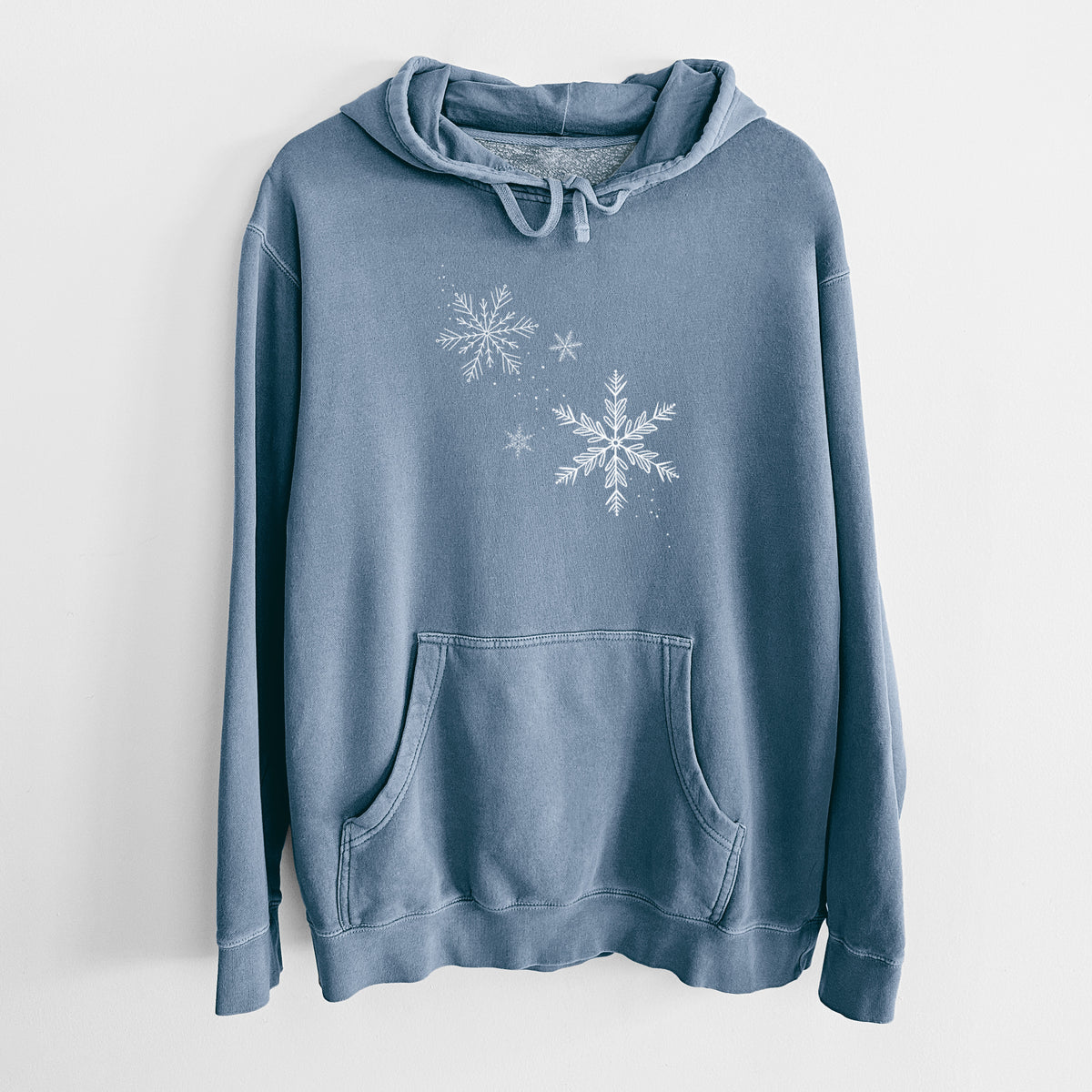 Slate blue pigment dyed hoodie laid flat, printed with delicate white snowflakes of different sizes falling.