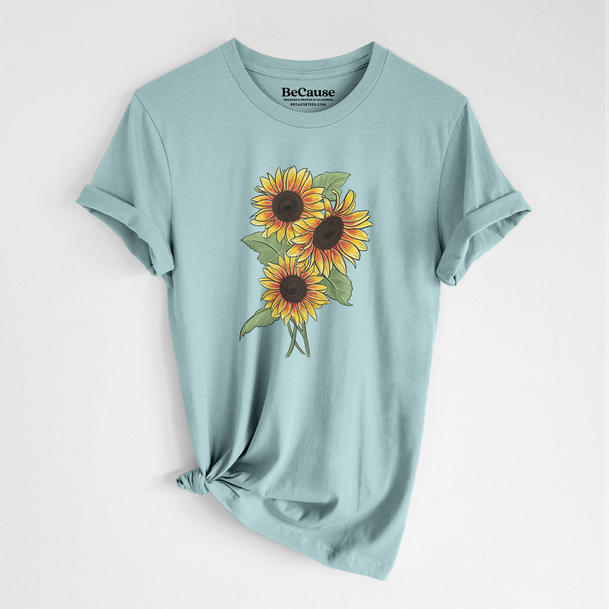 Dusty blue lightweight cotton t-shirt laid flat with the sleeves rolled, printed with a full-color illustration of a bunch of yellow and orange sunflowers.
