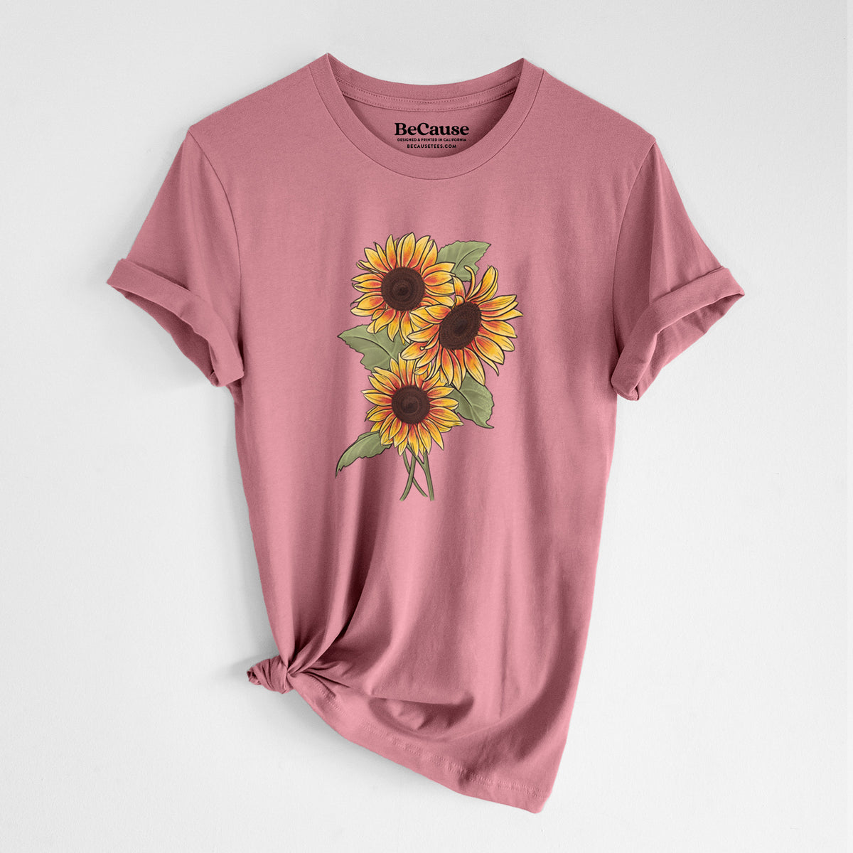 Mauve pink lightweight cotton t-shirt laid flat with the sleeves rolled, printed with a full-color illustration of a bunch of yellow and orange sunflowers.