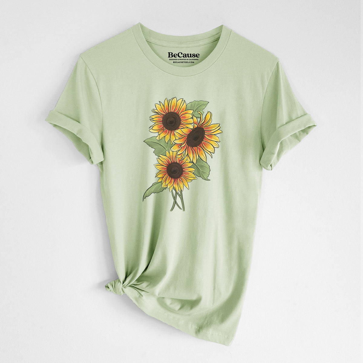 Spring green lightweight cotton t-shirt laid flat with the sleeves rolled, printed with a full-color illustration of a bunch of yellow and orange sunflowers.