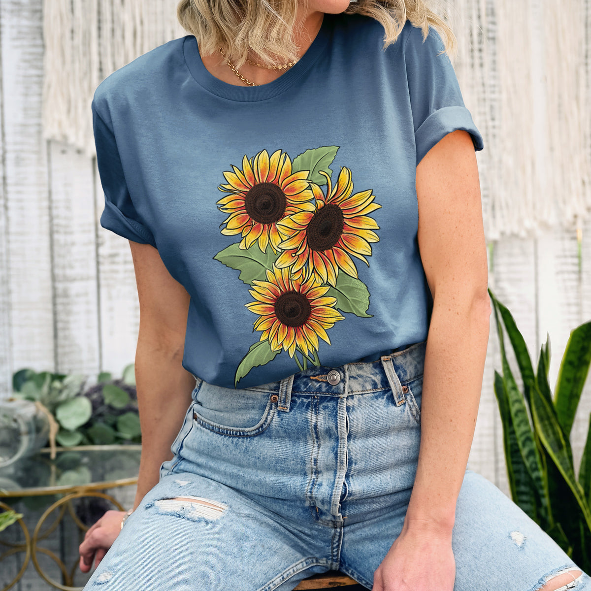 Woman wearing a steel blue lightweight cotton t-shirt printed with a full-color illustration of a bunch of yellow and orange sunflowers.