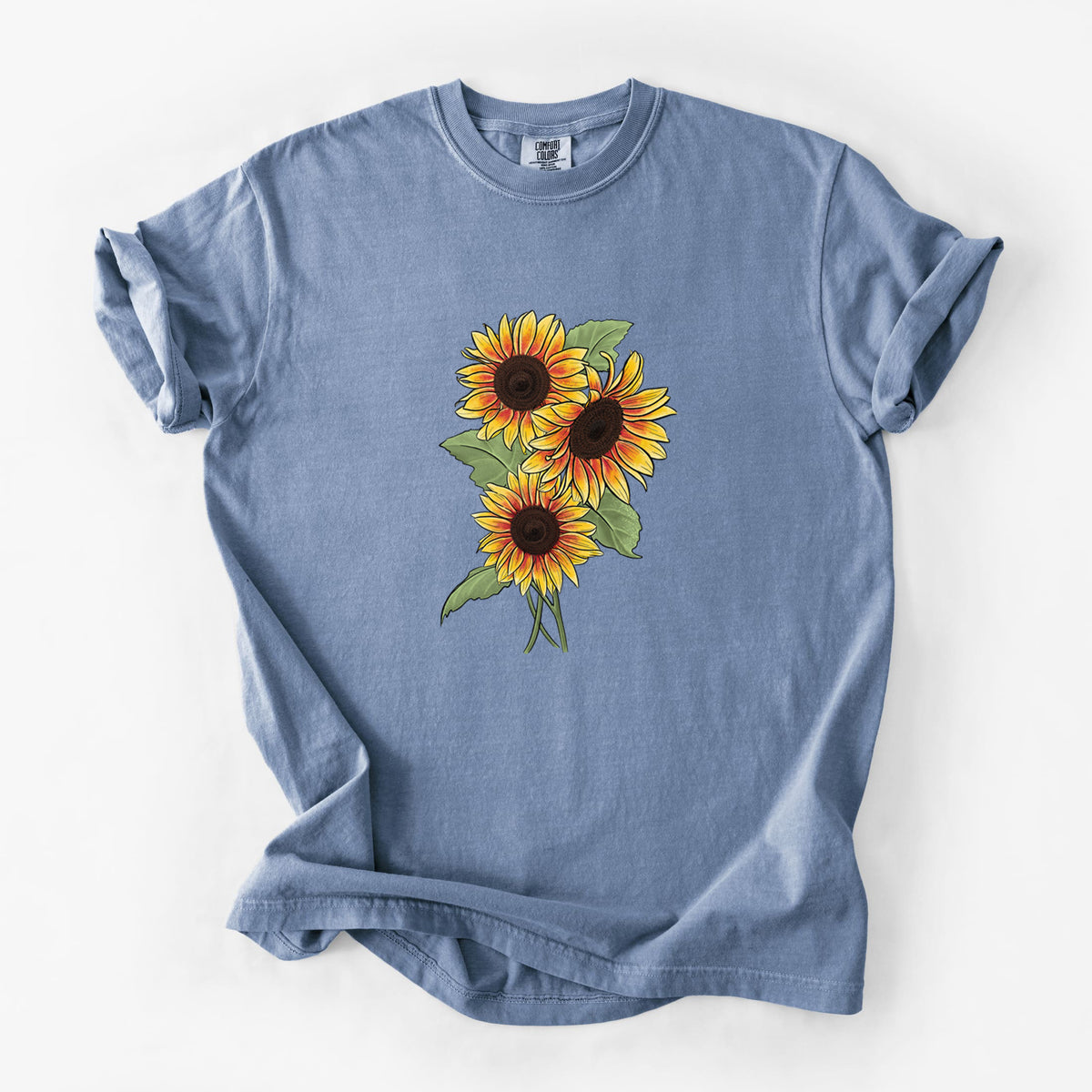 Blue jean Comfort Colors t-shirt laid flat, printed with a full-color illustration of a bunch of yellow and orange sunflowers.
