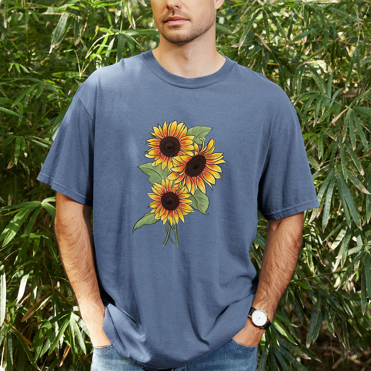 Man wearing a Comfort Colors t-shirt printed with a full-color illustration of a bunch of yellow and orange sunflowers, outdoors.