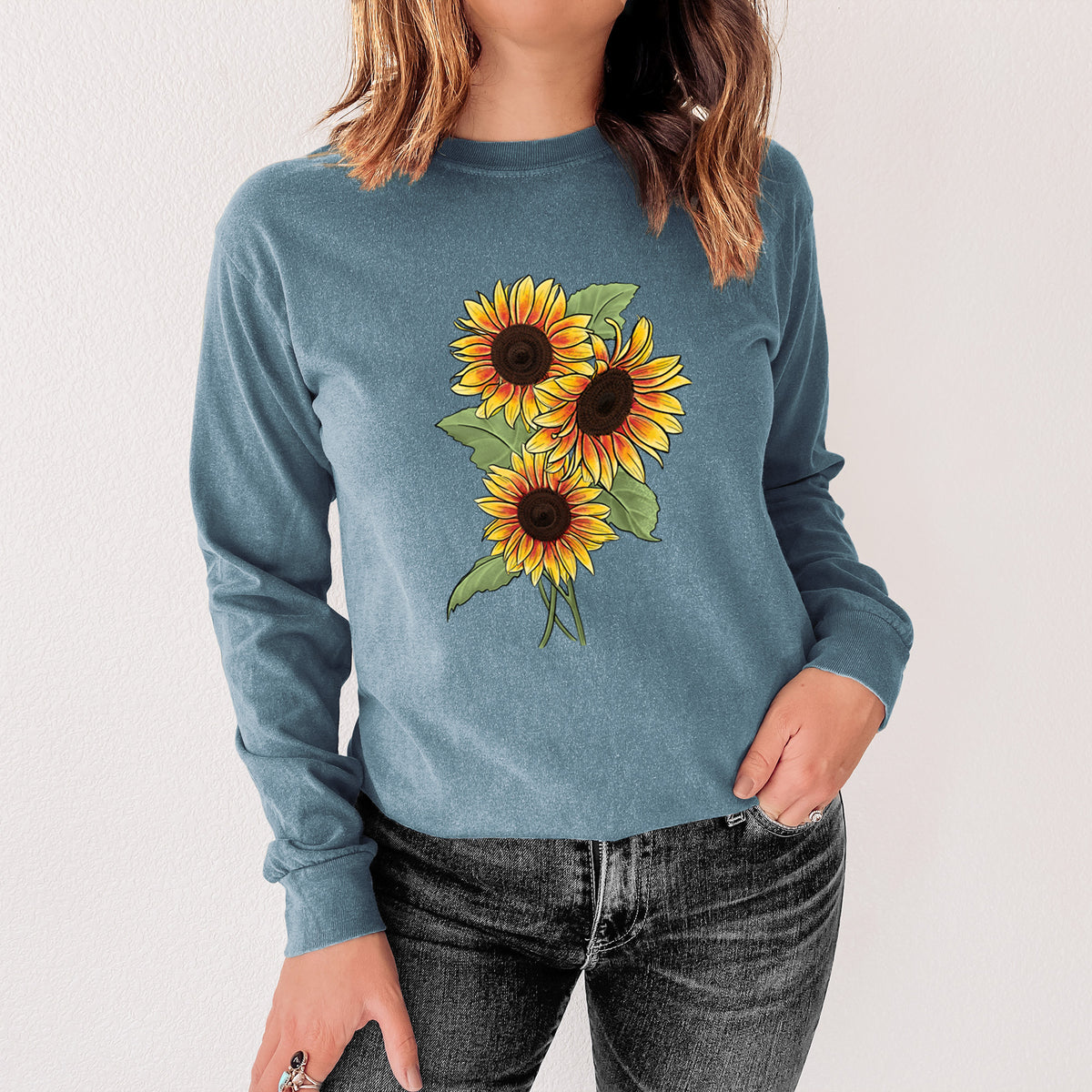 Steel blue Comfort Colors long sleeve shirt printed with a full-color illustration of a bunch of yellow and orange sunflowers, shown in a lifestyle photo.