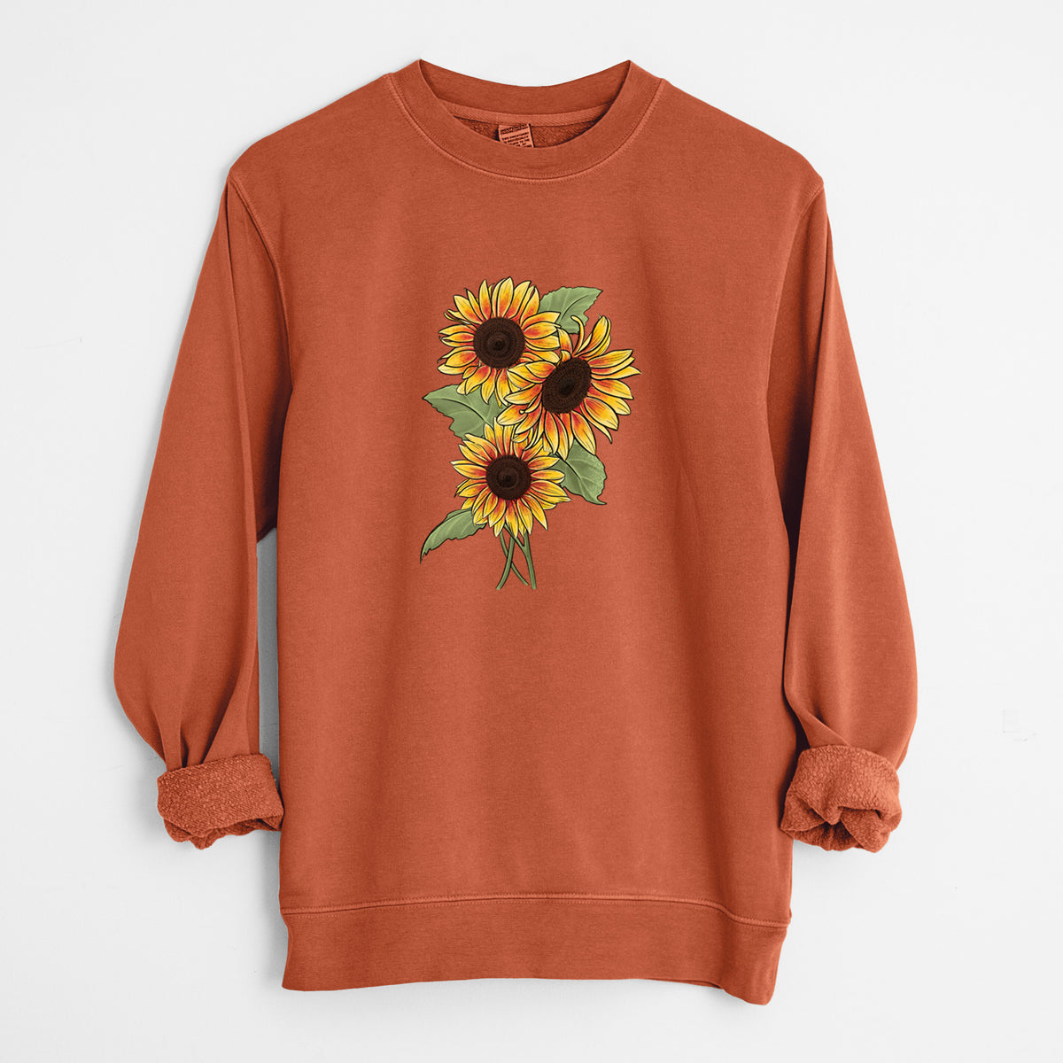 Amber orange pigment dyed crewneck sweatshirt laid flat with the sleeves rolled, printed with a full-color illustration of a bunch of yellow and orange sunflowers.