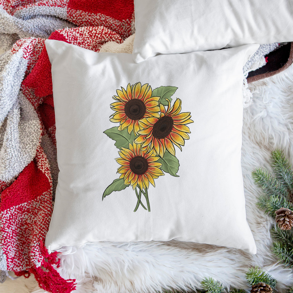 White pillow cover printed with a full-color illustration of a bunch of yellow and orange sunflowers, on a woven chair.