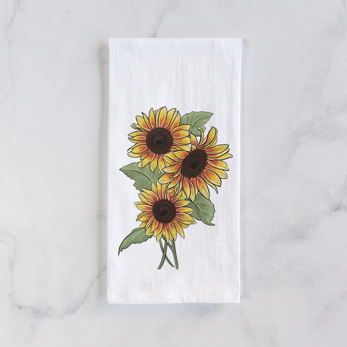 White cotton tea towel laid flat on marble, printed with a full-color illustration of a bunch of yellow and orange sunflowers.
