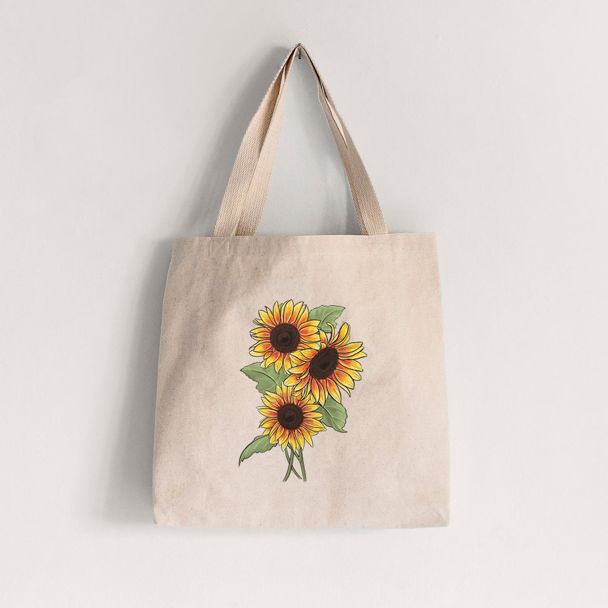 Natural canvas tote bag printed with a full-color illustration of a bunch of yellow and orange sunflowers.