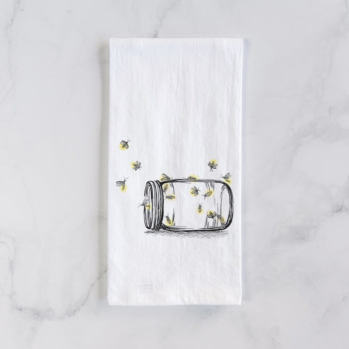 White cotton tea towel laid flat on marble, printed with a mason jar with glowing yellow fireflies flying out of it.