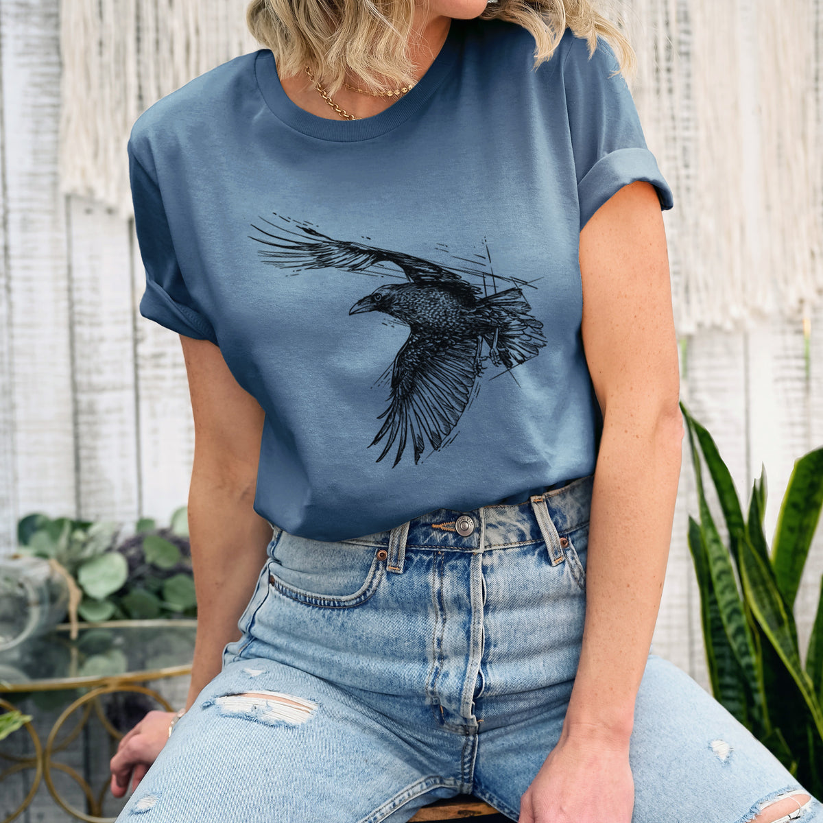 Woman wearing a steel blue lightweight cotton t-shirt printed with a black ink illustration of a raven in flight with its wings spread.