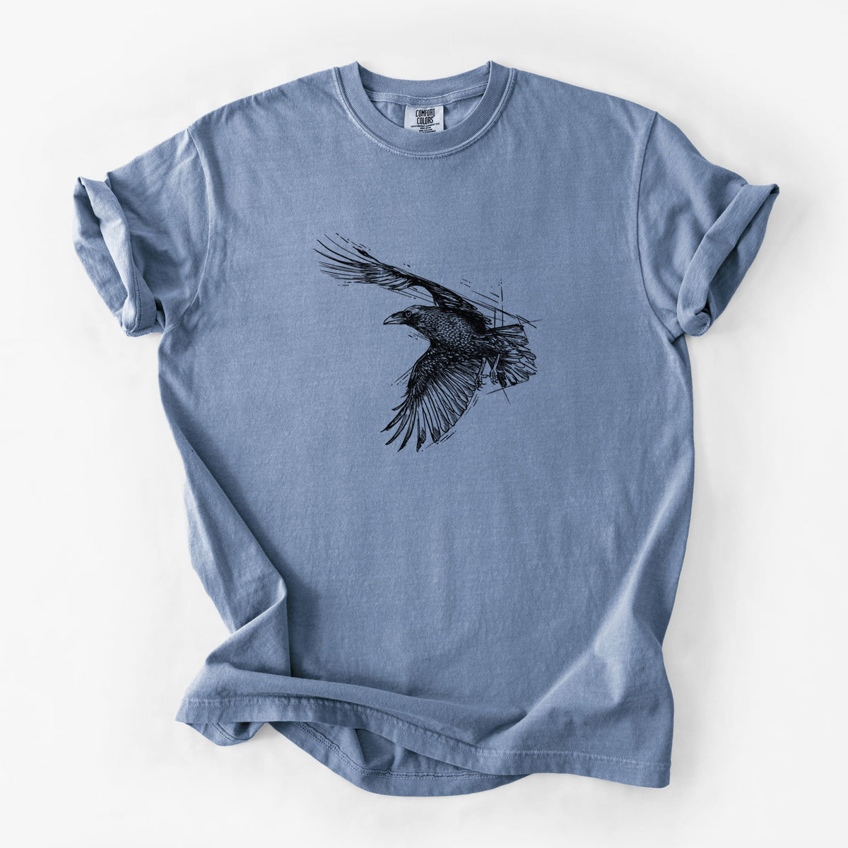 Blue jean Comfort Colors t-shirt laid flat, printed with a black ink illustration of a raven in flight with its wings spread.