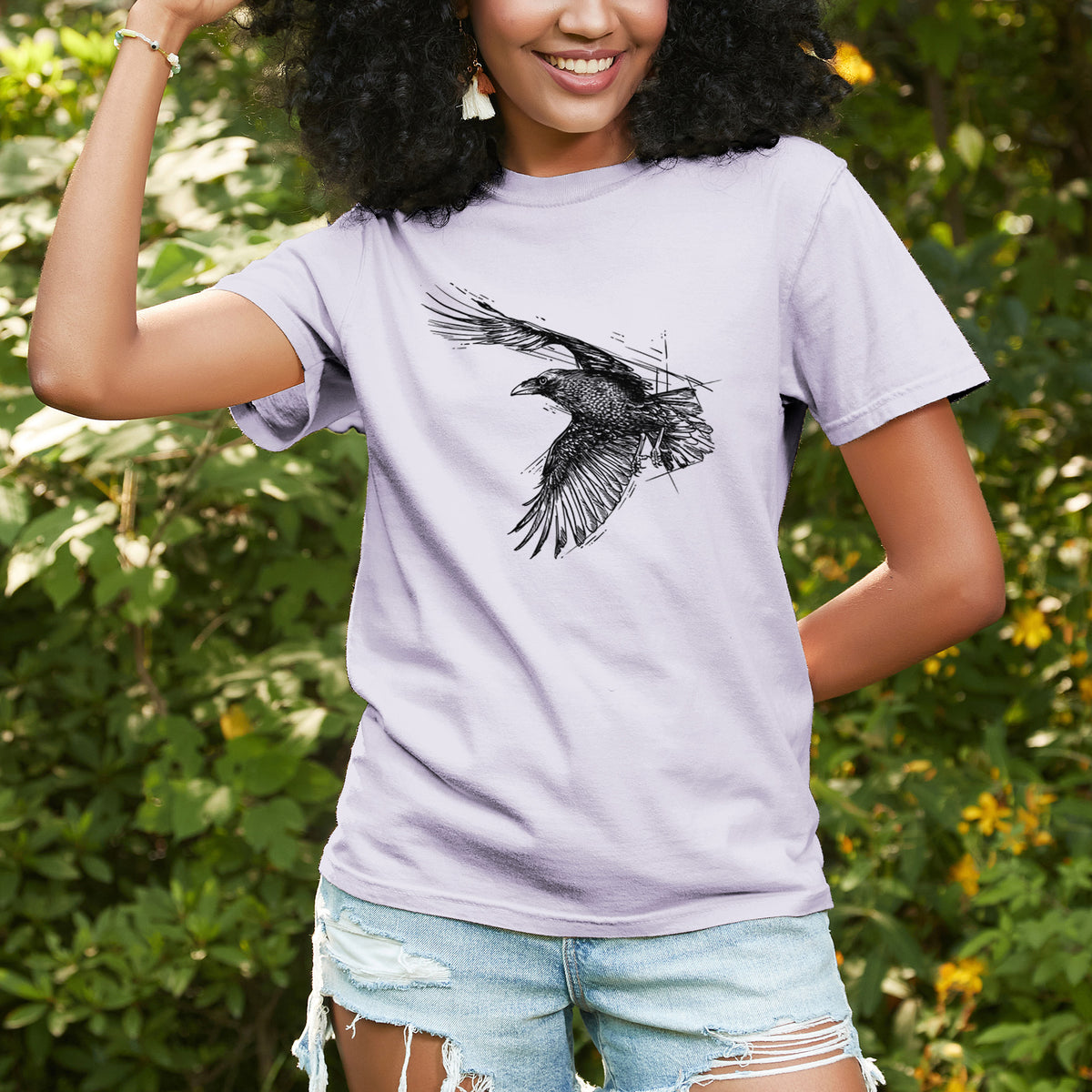 Woman wearing a Comfort Colors t-shirt printed with a black ink illustration of a raven in flight with its wings spread, outdoors.