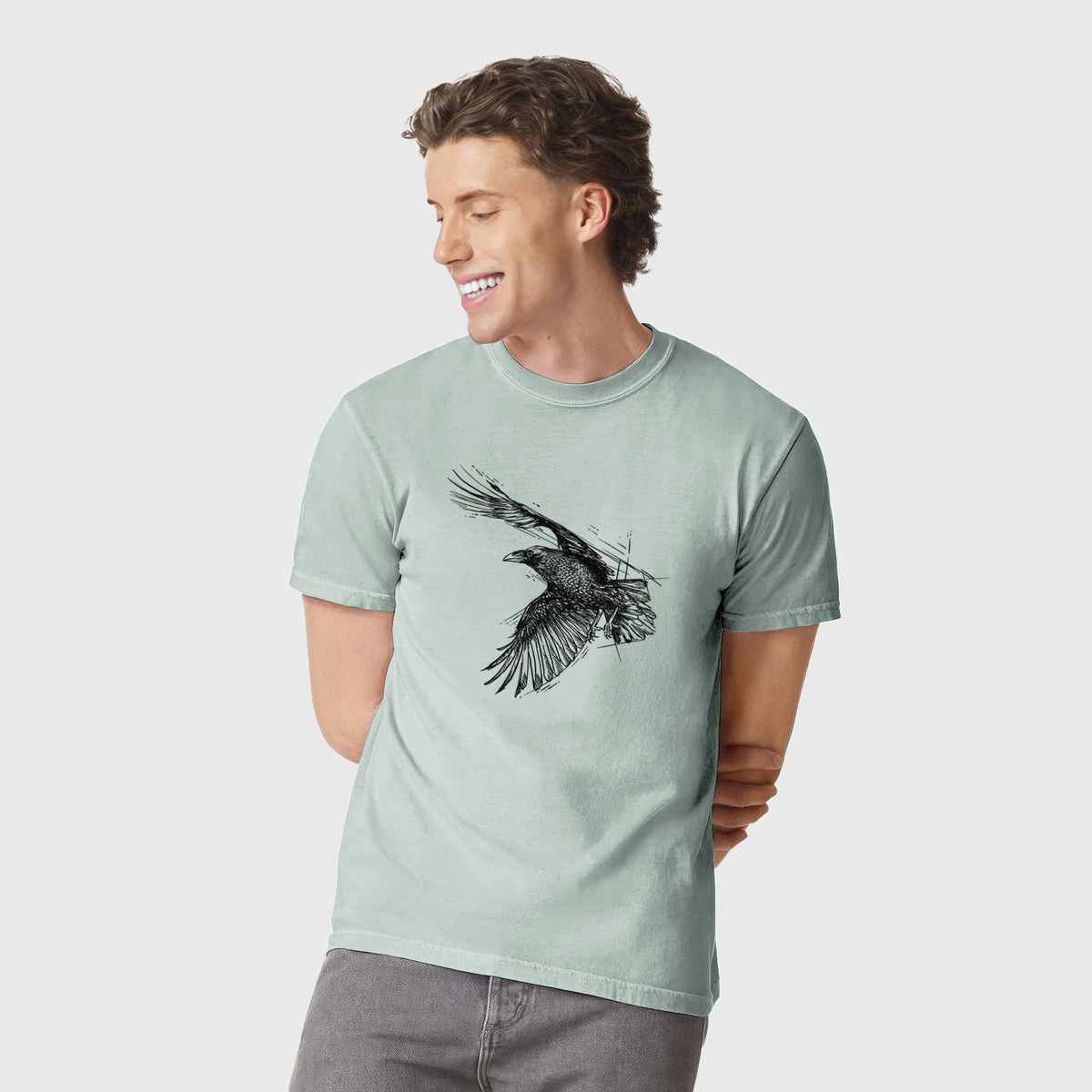 Man wearing a Comfort Colors t-shirt printed with a black ink illustration of a raven in flight with its wings spread.